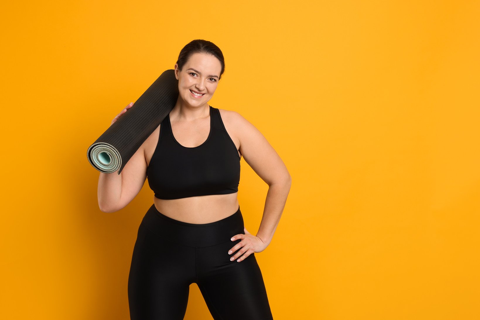 Happy overweight woman with yoga mat on orange background, space for text